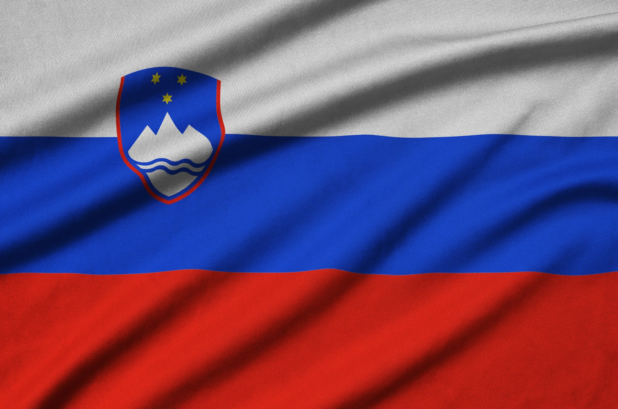 Slovenia flag is depicted on a sports cloth fabric with many folds. Sport team waving banner